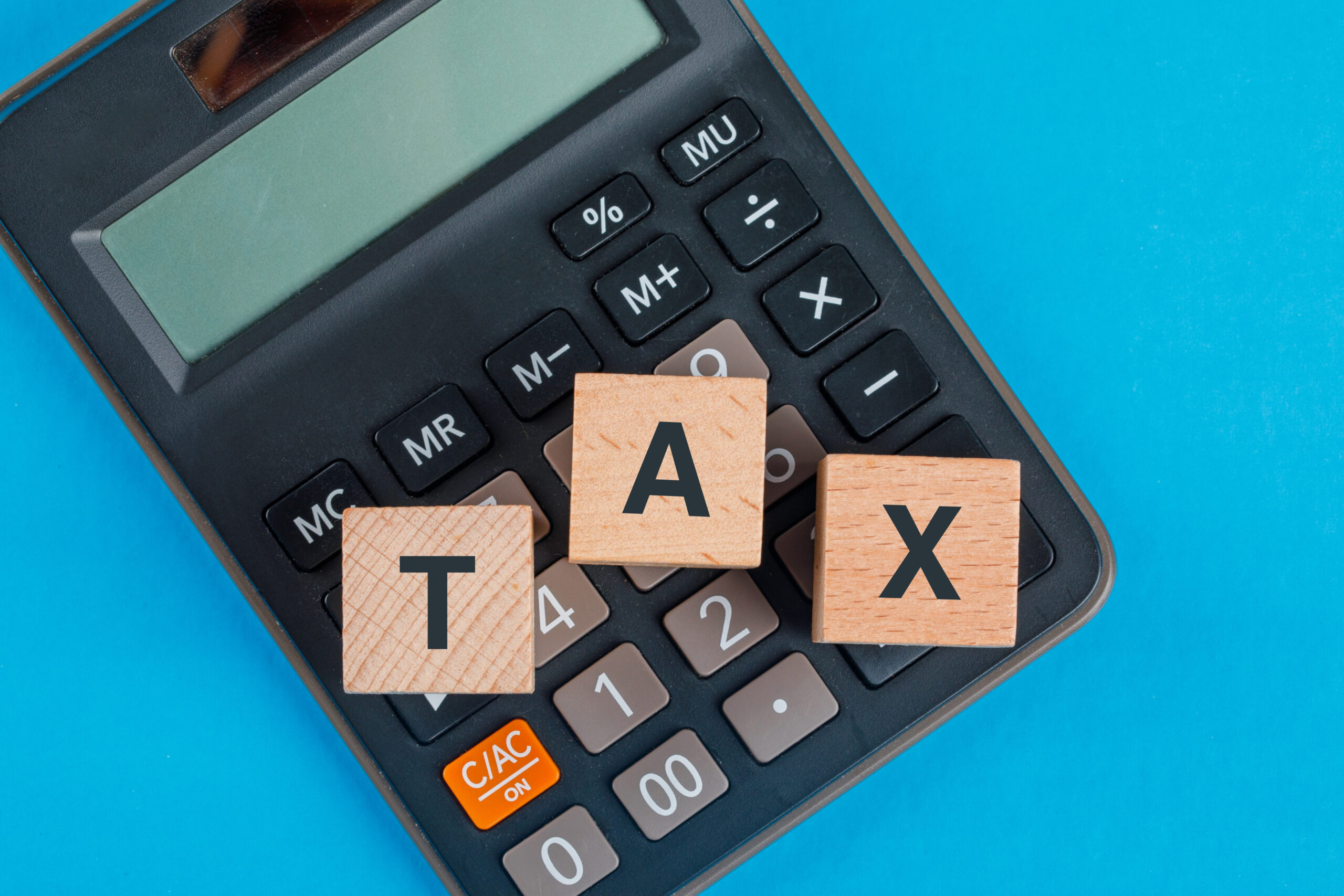 Tax planning concept with wooden cubes on calculator on blue background flat lay